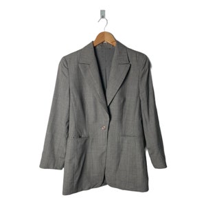 Puede incluir: Una chaqueta gris con un cierre de botón único y dos bolsillos de solapa. La chaqueta tiene un patrón de rayas finas.