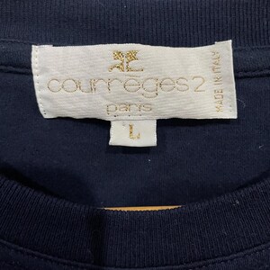 Op de afbeelding: Een marineblauw T-shirt met een wit label waarop "Courr&egrave;ges 2 Paris" en "Made in Italy" staat. Het label heeft ook een klein gouden logo van een gestileerde "C".