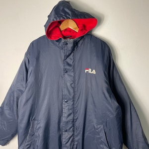 Pu&ograve; includere: Una giacca imbottita con cappuccio blu navy con fodera rossa e un logo FILA bianco sul davanti.