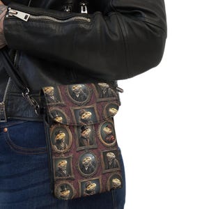 May include: A crossbody bag featuring a repeating pattern of bearded dragons dressed in formal Victorian-style clothing, each enclosed within an ornate, dark-toned oval or rectangular picture frame against a deep burgundy background.