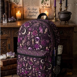 May include: A black backpack featuring a repeating pattern of purple roses, crystal balls, crescent moons, candles, and feathers. The bag includes a front zippered pocket, a top handle, and side mesh pockets containing a pen and a bundle of dried herbs.