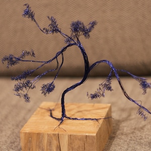 Puede incluir: Una escultura de alambre de un árbol con un acabado metálico azul. El árbol está sobre una base de madera.