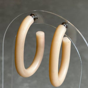 Op de afbeelding: Een paar crèmekleurige creolen. De oorbellen zijn gemaakt van een glad, afgerond materiaal en hebben een eenvoudig, elegant ontwerp.