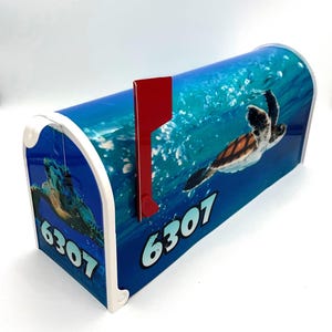 May include: A blue mailbox with a sea turtle design and the number 6307. The mailbox has a red flag.