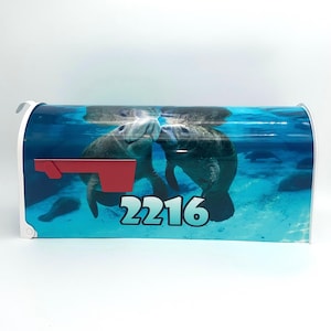 May include: A white mailbox with a blue and green underwater scene featuring two manatees. The mailbox has a red flag and the number 2216 printed on the front.