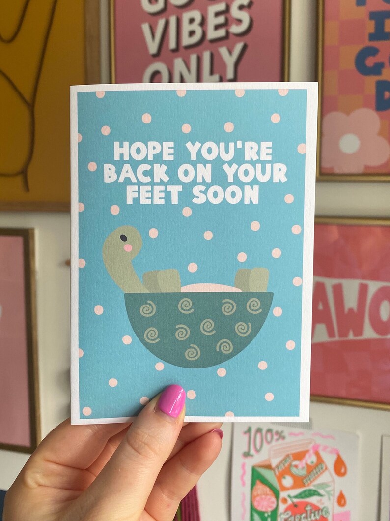 May include: A blue and white card with pink polka dots. The card features a cartoon turtle in a bowl and the text "Hope you're back on your feet soon."