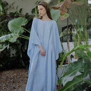 K&ouml;nnte beinhalten: Ein hellblaues Maxikleid mit einer lockeren, flie&szlig;enden Silhouette. Das Kleid hat einen runden Ausschnitt und lange &Auml;rmel. Das Model tr&auml;gt das Kleid mit Sandalen und einem Stirnband.