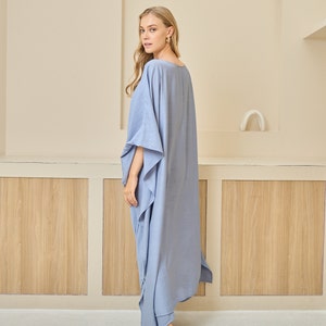 May include: A floor-length, periwinkle blue kaftan dress featuring a wide, loose-fitting silhouette with batwing sleeves, a simple round neckline, and side slits that extend from the hemline, creating a flowing and relaxed drape.