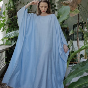 K&ouml;nnte beinhalten: Ein hellblaues Maxikleid mit einer lockeren, flie&szlig;enden Silhouette. Das Kleid hat einen runden Ausschnitt und lange &Auml;rmel. Das Model tr&auml;gt das Kleid mit einem Stirnband und Sandalen.