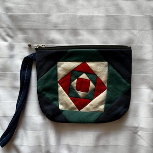May include: A small, blue, green, red, and white patchwork fabric zippered pouch with a black strap.