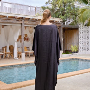 Peut inclure: Longue robe caftan noire &agrave; manches larges. La robe est faite d'un tissu fluide et est port&eacute;e &agrave; l'ext&eacute;rieur pr&egrave;s d'une piscine. La personne est dos &agrave; la cam&eacute;ra.
