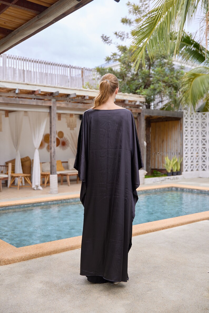Peut inclure: Longue robe caftan noire &agrave; manches larges. La robe est faite d'un tissu fluide et est port&eacute;e &agrave; l'ext&eacute;rieur pr&egrave;s d'une piscine. La personne est dos &agrave; la cam&eacute;ra.