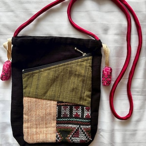 May include: A black patchwork crossbody bag with a zippered pocket and a long pink strap. The bag has a geometric pattern with green, brown, and white fabric.