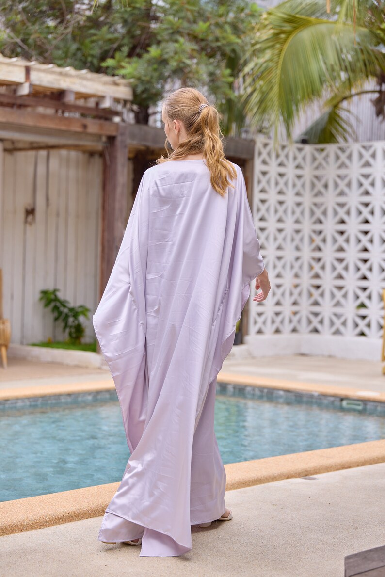 Puede incluir: Una mujer con un vestido largo y fluido de color lila claro estilo caft&aacute;n. Est&aacute; de pie junto a una piscina.