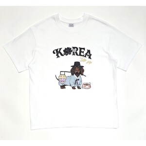May include: White t-shirt featuring a black and white illustration of a dachshund wearing traditional Korean attire, including a hat. The text "KOREA" and "Yo yo yip" is printed on the shirt.