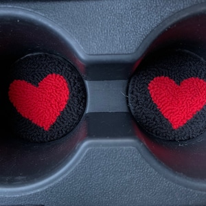 Peut inclure: Deux porte-gobelets de voiture noirs avec des inserts en forme de c&oelig;ur rouge. Les c&oelig;urs sont faits d'un mat&eacute;riau duveteux.