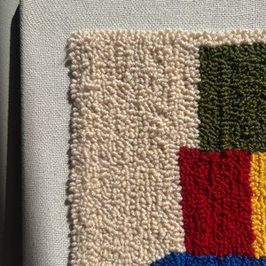 K&ouml;nnte beinhalten: Nahaufnahme eines bunten Teppichs mit einem geometrischen Muster in Creme, Gr&uuml;n, Rot, Blau und Gelb. Der Teppich ist aus Garn gefertigt und hat eine strukturierte Oberfl&auml;che.