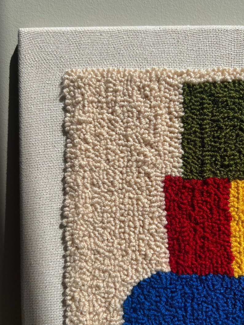 K&ouml;nnte beinhalten: Nahaufnahme eines bunten Teppichs mit einem geometrischen Muster in Creme, Gr&uuml;n, Rot, Blau und Gelb. Der Teppich ist aus Garn gefertigt und hat eine strukturierte Oberfl&auml;che.