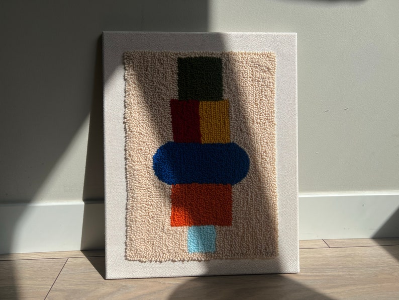 K&ouml;nnte beinhalten: Abstrakte Wandkunst mit einem Stapel bunter geometrischer Formen, darunter ein gr&uuml;nes Quadrat, rote und gelbe Rechtecke, ein blaues Oval und ein orangefarbenes Rechteck, alles auf einem beigefarbenen Hintergrund.