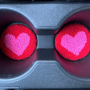 Peut inclure: Deux dessous-de-verre en forme de c&oelig;ur rouge et rose dans le porte-gobelet d'une voiture.