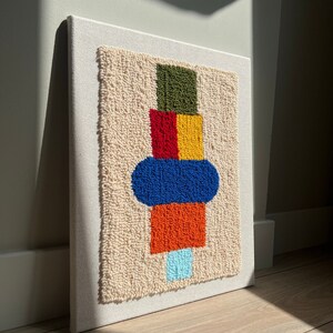 K&ouml;nnte beinhalten: Ein farbenfroher abstrakter Wandbehang mit einem geometrischen Design in Gr&uuml;n, Rot, Gelb, Blau, Orange und Hellblau. Das Design ist aus Garn gefertigt und auf einer wei&szlig;en Leinwand montiert.