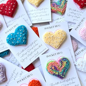 May include: A collection of colourful heart-shaped plush ornaments with the text "Pocket Hug" and a message about love and hugs.