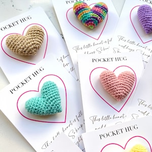 May include: A set of six crocheted heart-shaped pocket hug cards. Each card features a different color heart and the text "Pocket Hug" and a message about keeping the heart close.