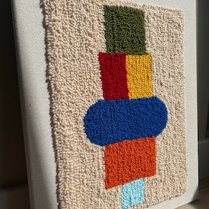 K&ouml;nnte beinhalten: Eine beige Leinwand mit einem farbenfrohen geometrischen Design. Das Design zeigt ein gr&uuml;nes Quadrat, ein rotes und gelbes Quadrat, ein blaues Oval, ein orangefarbenes Quadrat und ein hellblaues Oval.