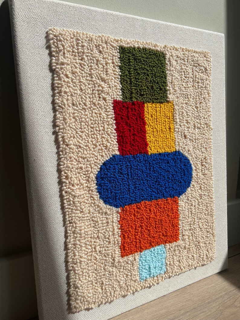 K&ouml;nnte beinhalten: Eine beige Leinwand mit einem farbenfrohen geometrischen Design. Das Design zeigt ein gr&uuml;nes Quadrat, ein rotes und gelbes Quadrat, ein blaues Oval, ein orangefarbenes Quadrat und ein hellblaues Oval.