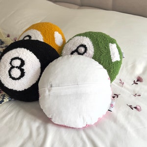May include: Four round pillows with a white background and a black number eight on each. The pillows are in the colors black, yellow, green, and pink.