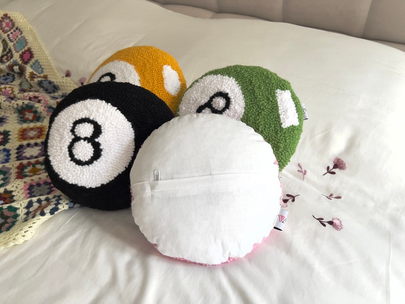 May include: Four round pillows with a white background and a black number eight on each. The pillows are in the colors black, yellow, green, and pink.