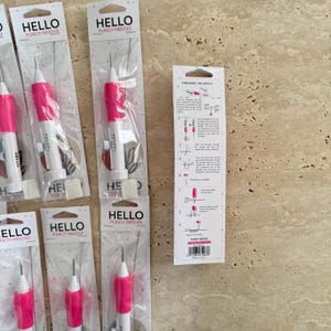 May include: A close-up of ten pink and white punch needles with the text "HELLO PUNCH NEEDLE" on the packaging. Instructions for threading the needle are included on a separate card.