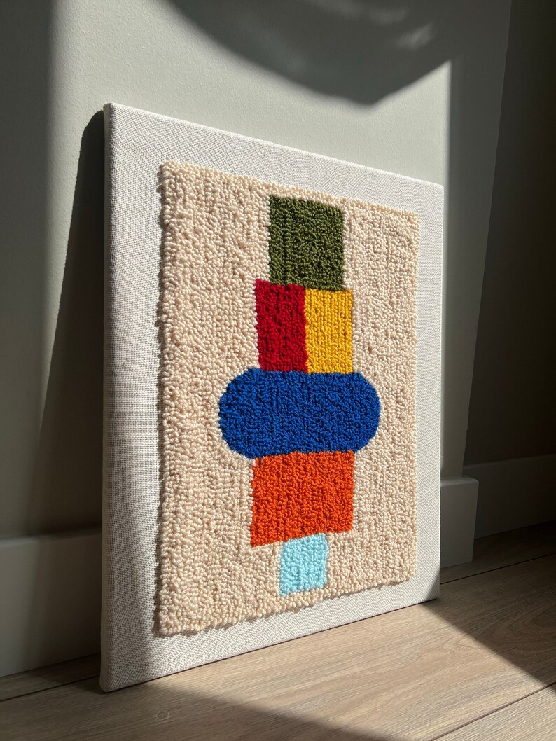 K&ouml;nnte beinhalten: Ein farbenfrohes abstraktes geometrisches Design wird mit Garn auf einer wei&szlig;en Leinwand geschaffen. Das Design zeigt gr&uuml;ne, rote, gelbe, blaue, orangefarbene und hellblaue Quadrate und Kreise.