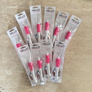 May include: Ten pink and white punch needles individually packaged in clear plastic bags. Each package has the text "HELLO PUNCH NEEDLE" printed on it.