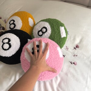 May include: Four plush pillows shaped like pool balls, each with a white number eight on a different colored background: black, yellow, green, and pink.