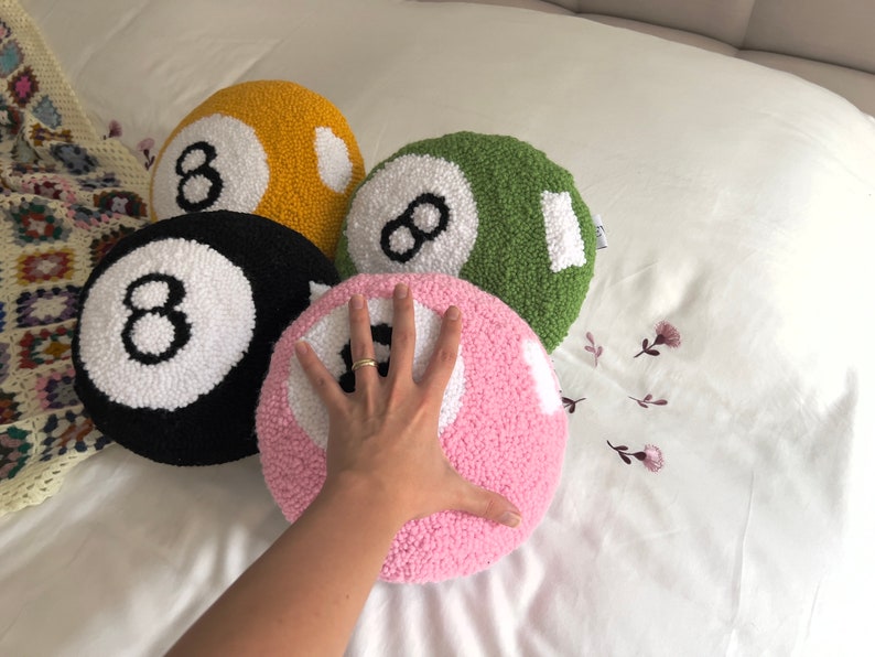 May include: Four plush pillows shaped like pool balls, each with a white number eight on a different colored background: black, yellow, green, and pink.