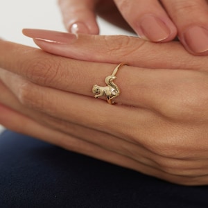 以下が含まれることがあります： リスのデザインの金の指輪。リスは後ろ足で座り、尻尾を丸めています。