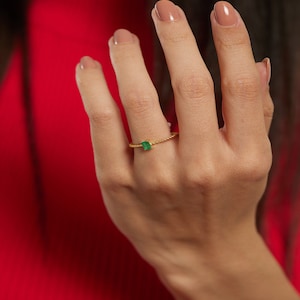 May include: A gold ring with a small emerald green gemstone. The ring has a twisted band.