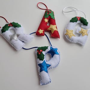 May include: Felt Christmas decorations spelling "GAP". The letters are white, red, and blue, with glittery accents and star details. Each letter has a loop for hanging, perfect for festive decor.