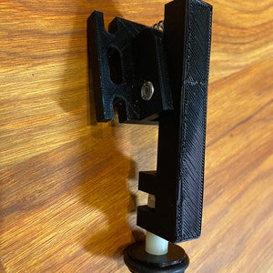 May include: A black 3D printed object with a white plastic rod and a black rubber ring. The object has a lever and a spring.