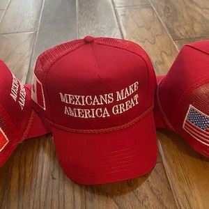 May include: Three red mesh trucker hats with different embroidered designs. One hat features the text "Mexicans Make America Great" and a small Canadian flag. Another hat features a Mexican flag. The third hat features a small American flag.