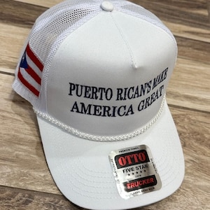 May include: White trucker hat with a mesh back. The hat has a red, white, and blue Puerto Rican flag patch on the side and the text "PUERTO RICAN'S MAKE AMERICA GREAT" embroidered in blue on the front. The hat has a black and silver label with the text "OTTO FIVE STAR TRUCKER CLASSIC MESH BACK".