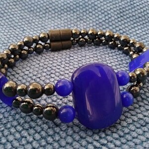 Könnte beinhalten: Ein Armband mit zwei Reihen schwarzer Perlen und einem großen, ovalen blauen Edelstein. Das Armband hat einen Magnetverschluss.