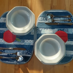 Könnte beinhalten: Zwei weiße achteckige Teller mit Perlenrand liegen auf Jeans-Tischsets mit roten Apfelapplikationen. Auf den Tischsets ist Besteck angeordnet, darunter Löffel, Gabeln und Messer, was eine rustikale Essumgebung schafft.