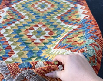 May include: A colorful woven rug with a geometric pattern in shades of red, orange, yellow, green, and blue. The rug has a fringe border and is folded in half.