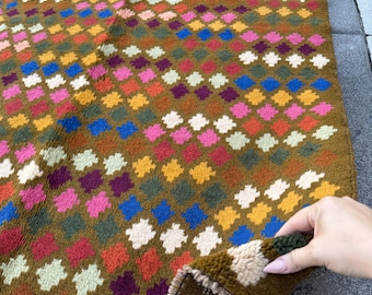 May include: A colorful, patterned rug with a repeating diamond design. The rug features a brown base with diamonds in various colors, including blue, pink, orange, and white. The rug's edges are finished with a brown border.