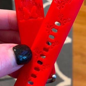 May include: Two red silicone watch bands with a Disney theme. One band features a silhouette of Cinderella's castle with the text "100" and the other band has a repeating pattern of Mickey Mouse heads.