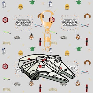 Puede incluir: Un llavero temático de Star Wars con un diseño del Halcón Milenario. El llavero tiene un cierre dorado y una imagen detallada de la nave espacial. El fondo es gris claro con personajes y logotipos de Star Wars.