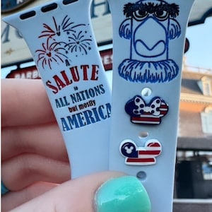 Op de afbeelding: Twee Apple Watch-bandjes met rood-wit-blauwe ontwerpen. Een bandje heeft een cartoon-arend met de tekst "A Salute to All Nations but mostly America". Het andere bandje heeft een cartoon-Minnie Mouse met een rood-wit-blauwe strik en een Mickey Mouse-hoofd met een rood-wit-blauw ontwerp.