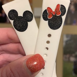 May include: Two white silicone watch bands with black and red glitter Mickey Mouse and Minnie Mouse designs. The bands have silver metal clasps.
